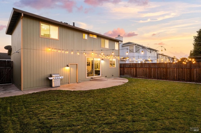 back house at dusk with a lawn and a patio