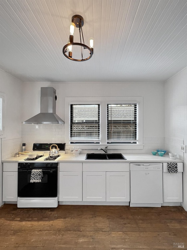 kitchen featuring white appliances, sink, wall chimney range hood, white cabinetry, and hanging light fixtures