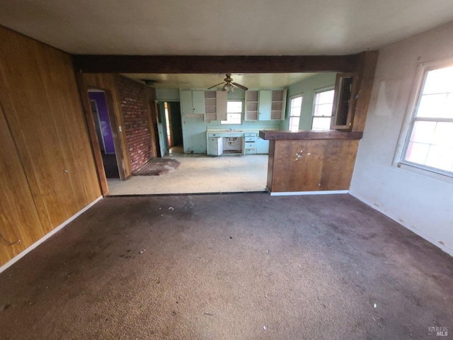 kitchen featuring beam ceiling, ceiling fan, wooden walls, and sink