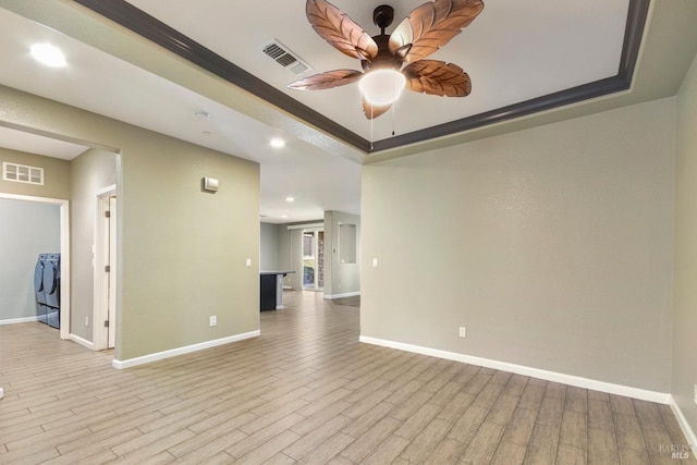 spare room with light hardwood / wood-style flooring, ceiling fan, independent washer and dryer, ornamental molding, and a tray ceiling