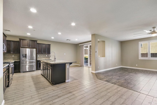 kitchen with dark brown cabinetry, sink, an island with sink, a kitchen bar, and appliances with stainless steel finishes