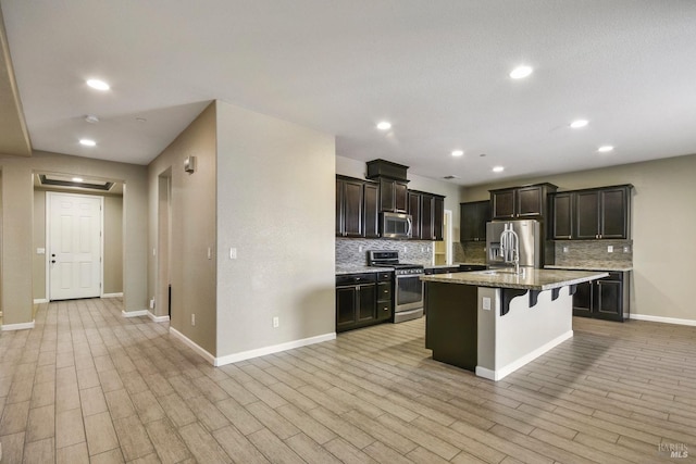 kitchen with light wood-type flooring, stainless steel appliances, a breakfast bar area, and an island with sink