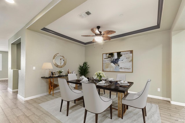 dining room with light hardwood / wood-style flooring, a raised ceiling, and ceiling fan