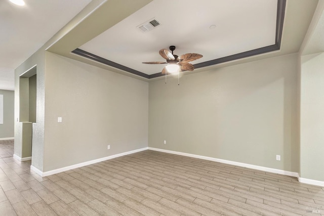 empty room featuring a raised ceiling, ceiling fan, and light wood-type flooring