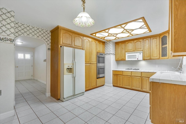 kitchen featuring tasteful backsplash, white appliances, sink, light tile patterned floors, and hanging light fixtures