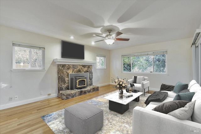 living room with a wealth of natural light, wood-type flooring, a wood stove, and ceiling fan