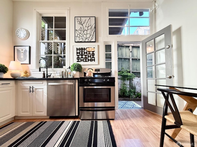 bar featuring appliances with stainless steel finishes, a wealth of natural light, a sink, and light wood finished floors