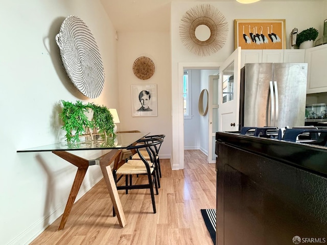 kitchen featuring baseboards, light wood-style floors, white cabinets, freestanding refrigerator, and gas stove