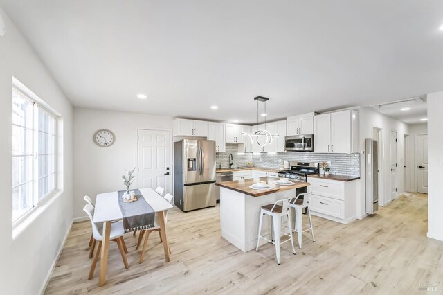 kitchen featuring white cabinetry, a center island, butcher block countertops, decorative light fixtures, and appliances with stainless steel finishes