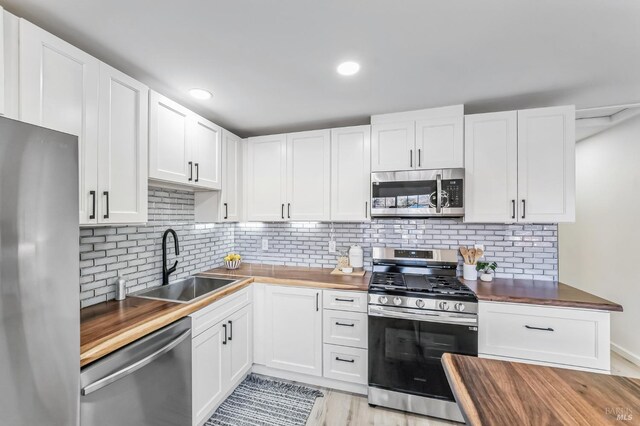 kitchen with wood counters, stainless steel appliances, white cabinetry, and sink