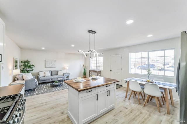 kitchen featuring a center island, appliances with stainless steel finishes, butcher block countertops, decorative light fixtures, and white cabinetry