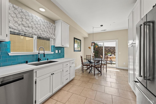 kitchen with decorative backsplash, stainless steel appliances, sink, white cabinets, and hanging light fixtures