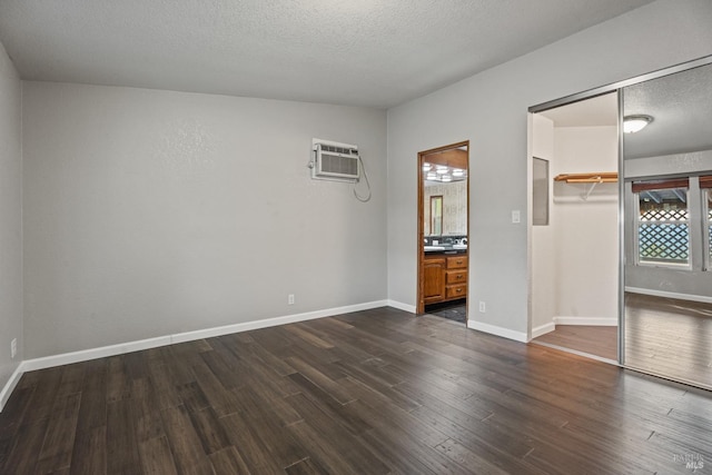 unfurnished bedroom with ensuite bathroom, a walk in closet, an AC wall unit, dark hardwood / wood-style floors, and a closet