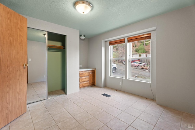 unfurnished bedroom with multiple windows, light tile patterned floors, a textured ceiling, and a closet