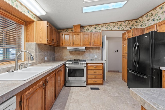 kitchen featuring sink, black fridge, lofted ceiling with skylight, decorative backsplash, and stainless steel stove