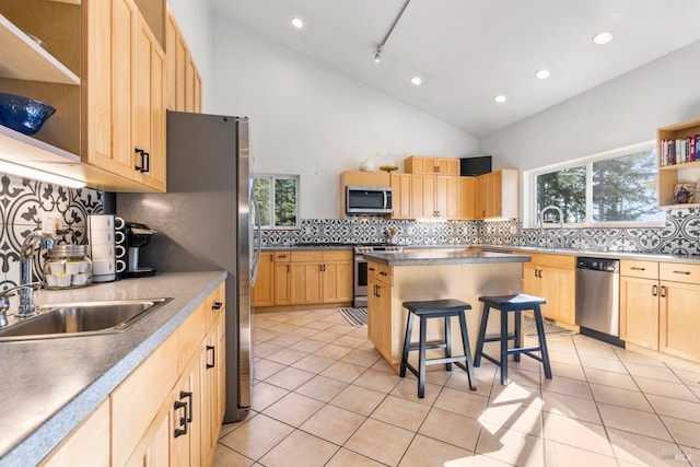 kitchen with a kitchen bar, light brown cabinetry, track lighting, stainless steel appliances, and sink