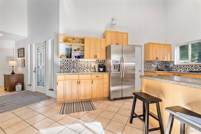 kitchen featuring decorative backsplash, stainless steel fridge with ice dispenser, light brown cabinets, and a high ceiling