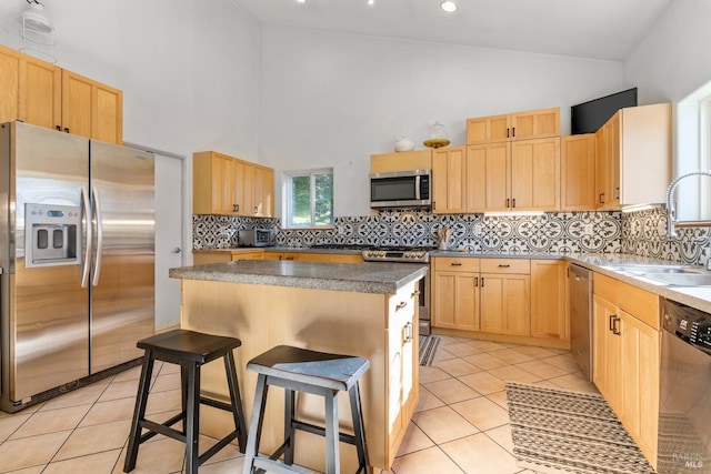 kitchen with appliances with stainless steel finishes, a kitchen breakfast bar, light brown cabinetry, sink, and a center island