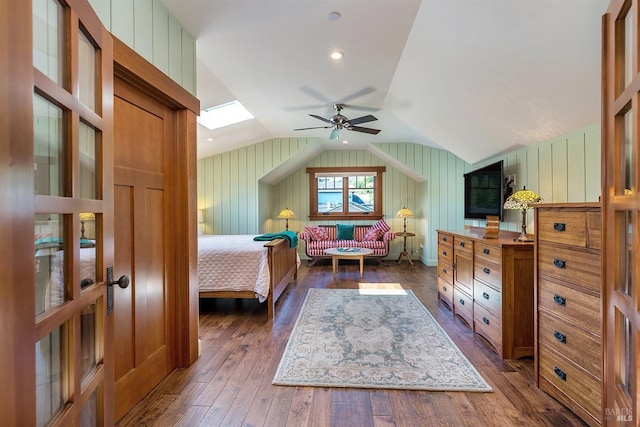 bedroom with ceiling fan, vaulted ceiling with skylight, dark wood-type flooring, and wooden walls