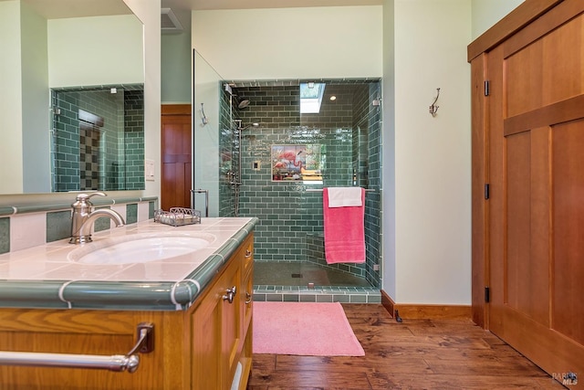 bathroom with hardwood / wood-style floors, vanity, and a tile shower