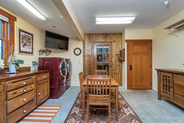 clothes washing area with washing machine and dryer, wood walls, and cabinets