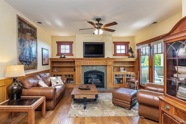 living room with ceiling fan, light wood-type flooring, wooden walls, and a tiled fireplace