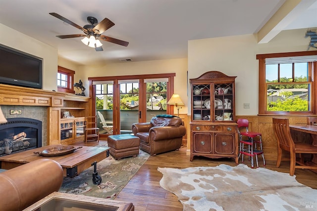 living room with a tile fireplace, ceiling fan, and wood-type flooring