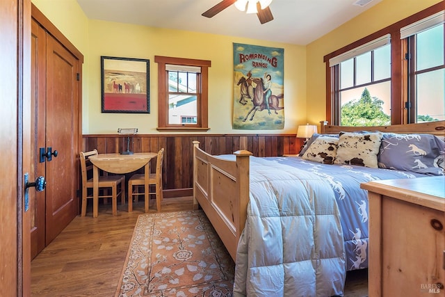 bedroom with ceiling fan, wood walls, and wood-type flooring