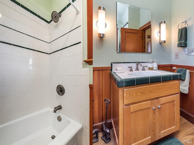 bathroom featuring wooden walls, vanity, tiled shower / bath combo, and hardwood / wood-style flooring