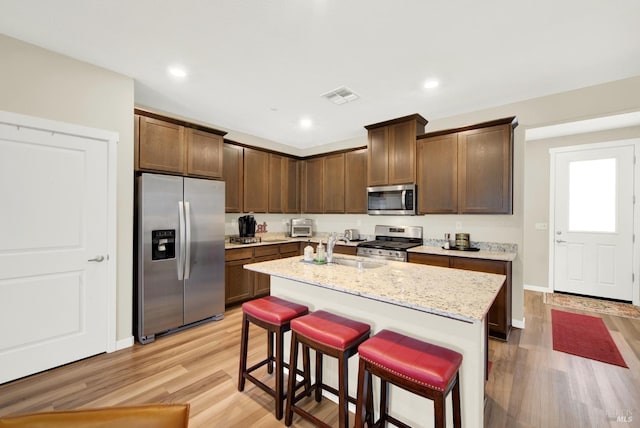 kitchen with a kitchen breakfast bar, sink, light stone countertops, an island with sink, and stainless steel appliances