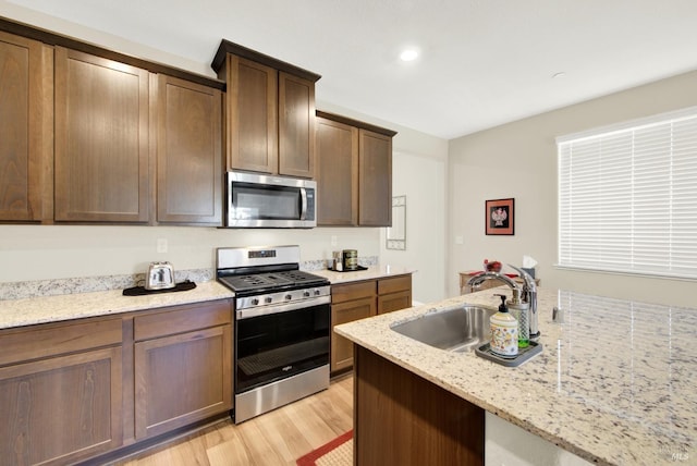 kitchen featuring sink, light wood-type flooring, light stone countertops, appliances with stainless steel finishes, and dark brown cabinets