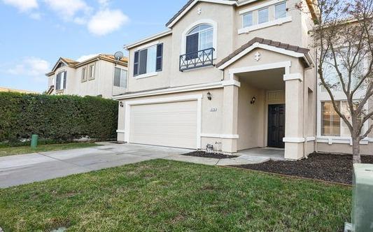 traditional-style home featuring a garage, driveway, a front lawn, and stucco siding