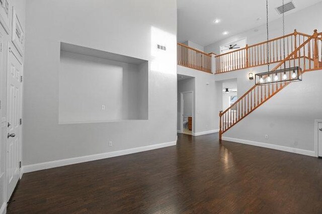 unfurnished living room with ceiling fan, dark hardwood / wood-style floors, and a towering ceiling