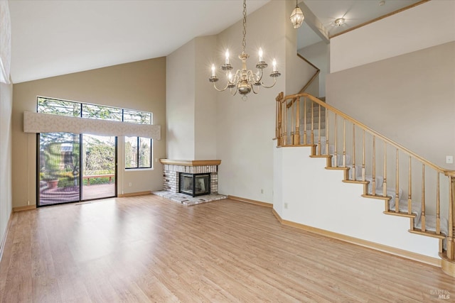 unfurnished living room featuring hardwood / wood-style floors, a towering ceiling, a chandelier, and a brick fireplace