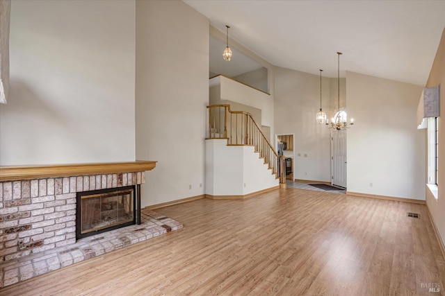 unfurnished living room featuring an inviting chandelier, hardwood / wood-style flooring, a brick fireplace, and lofted ceiling