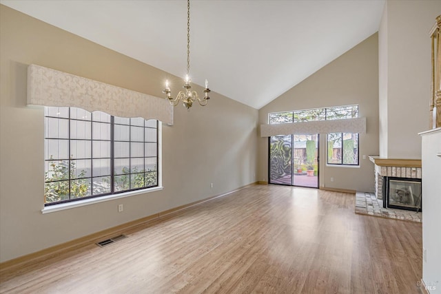 unfurnished living room with hardwood / wood-style flooring, plenty of natural light, an inviting chandelier, and a brick fireplace