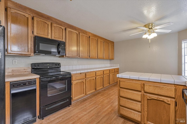 kitchen featuring tile countertops, black appliances, light hardwood / wood-style flooring, ceiling fan, and a textured ceiling