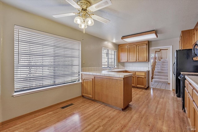 kitchen featuring tile countertops, black appliances, ceiling fan, light wood-type flooring, and kitchen peninsula