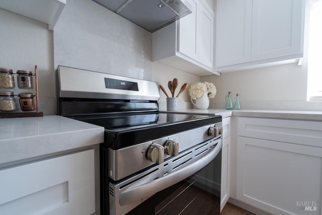 kitchen with exhaust hood, white cabinets, and stainless steel electric range oven