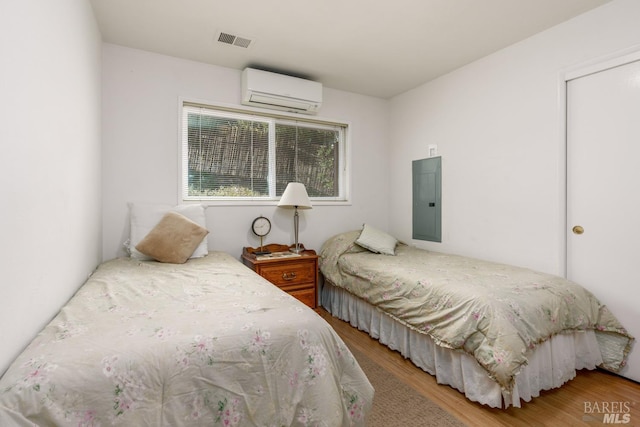 bedroom with hardwood / wood-style floors, an AC wall unit, and electric panel