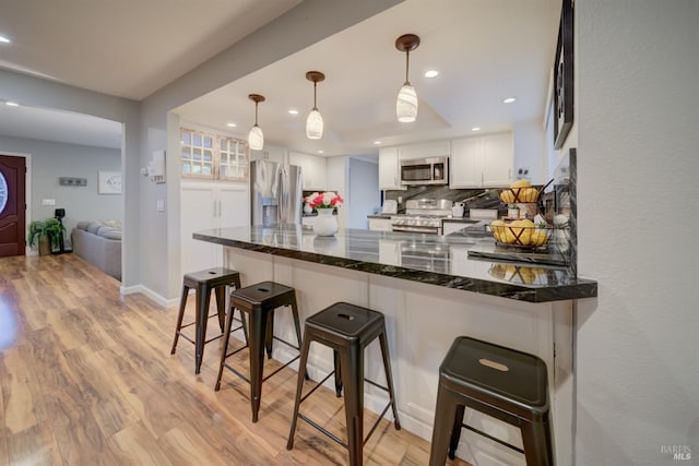 kitchen featuring kitchen peninsula, stainless steel appliances, dark stone countertops, white cabinetry, and hanging light fixtures