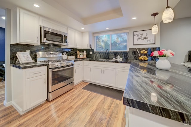 kitchen featuring stainless steel appliances, a tray ceiling, sink, pendant lighting, and white cabinetry