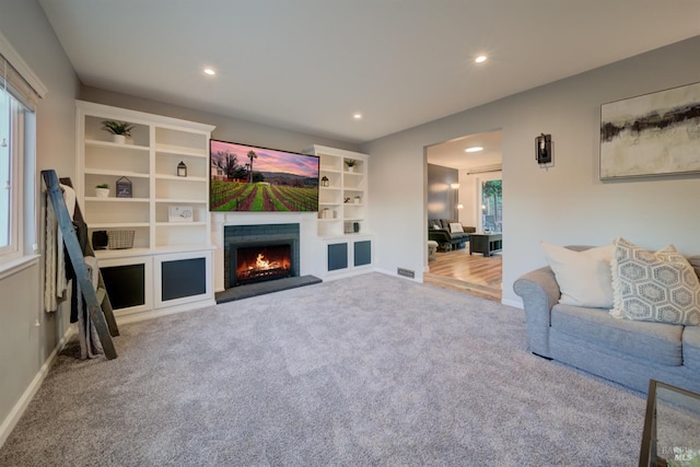 carpeted living room with a fireplace, built in features, and plenty of natural light