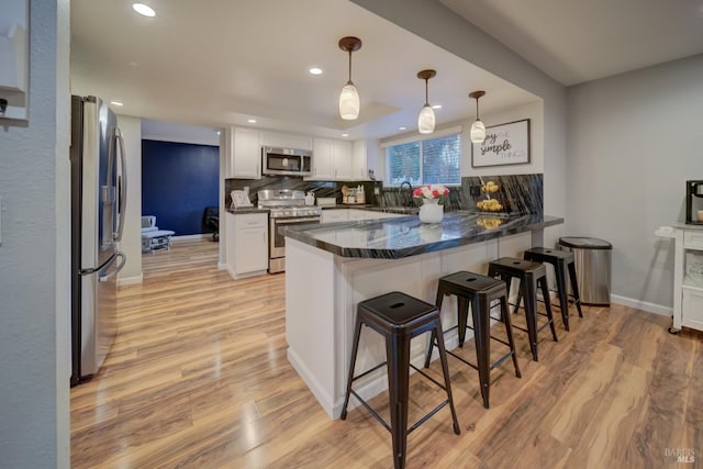 kitchen with a breakfast bar area, kitchen peninsula, white cabinetry, and appliances with stainless steel finishes