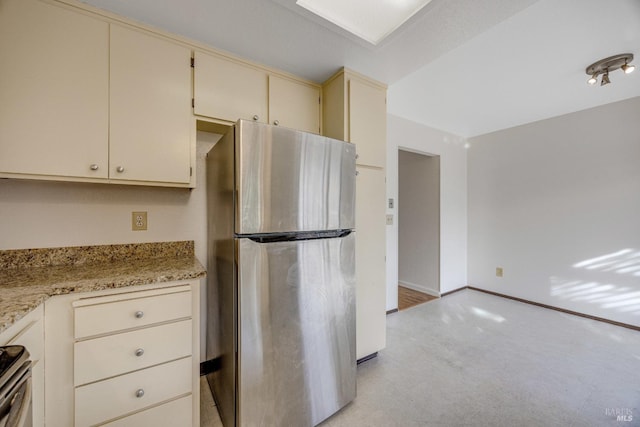 kitchen featuring cream cabinetry, stainless steel fridge, light carpet, and light stone countertops