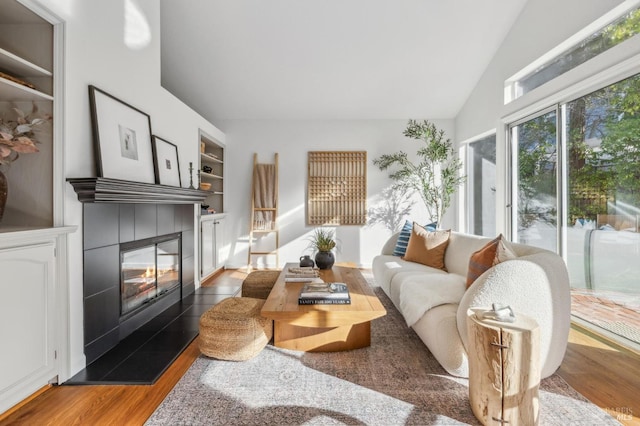 living room with lofted ceiling, wood-type flooring, built in shelves, and a tiled fireplace