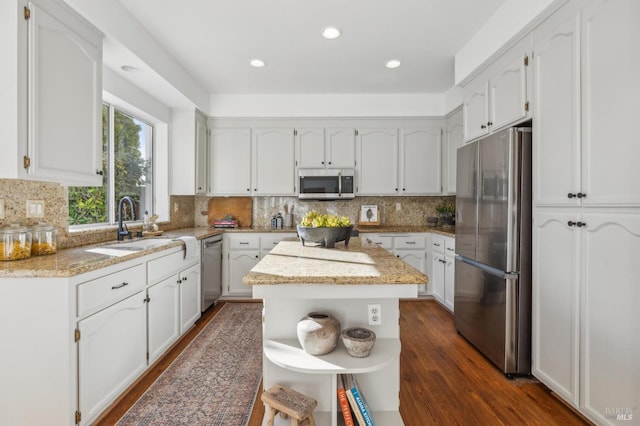 kitchen with white cabinetry, a center island, light stone countertops, dark hardwood / wood-style floors, and appliances with stainless steel finishes