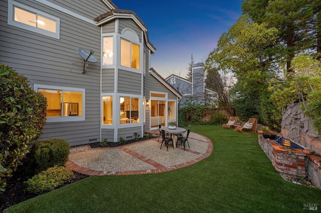 back house at dusk with a lawn and a patio area