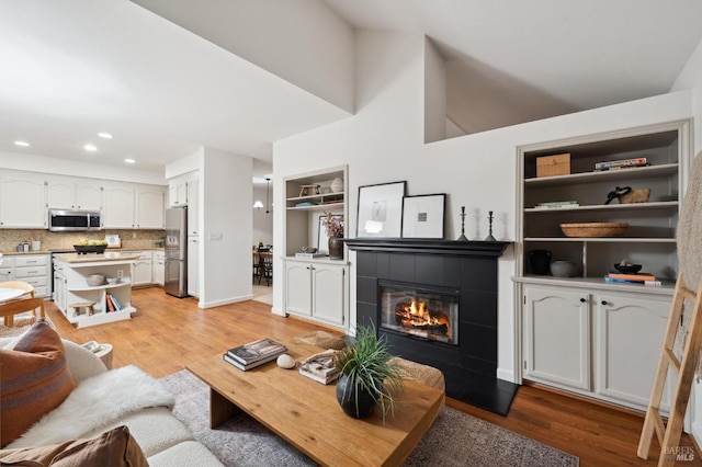 living room featuring built in shelves, a fireplace, and light hardwood / wood-style flooring