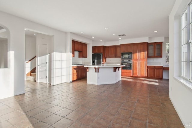 kitchen featuring a breakfast bar area, a center island with sink, black appliances, and tile patterned flooring